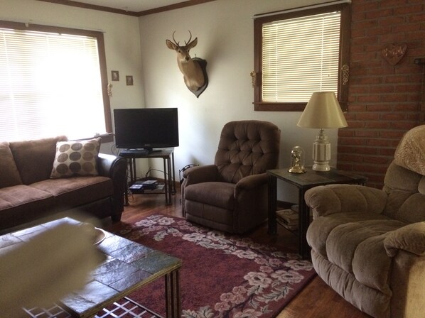 A living room with a sofa, armchair, television, and a mounted deer head.