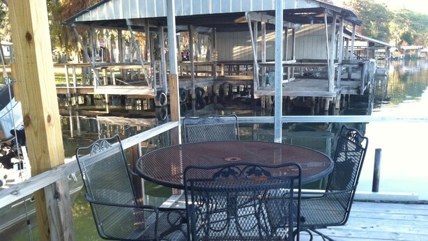 Une terrasse en bois avec une table ronde et des chaises, donnant sur une étendue d’eau où sont amarrés des bateaux.