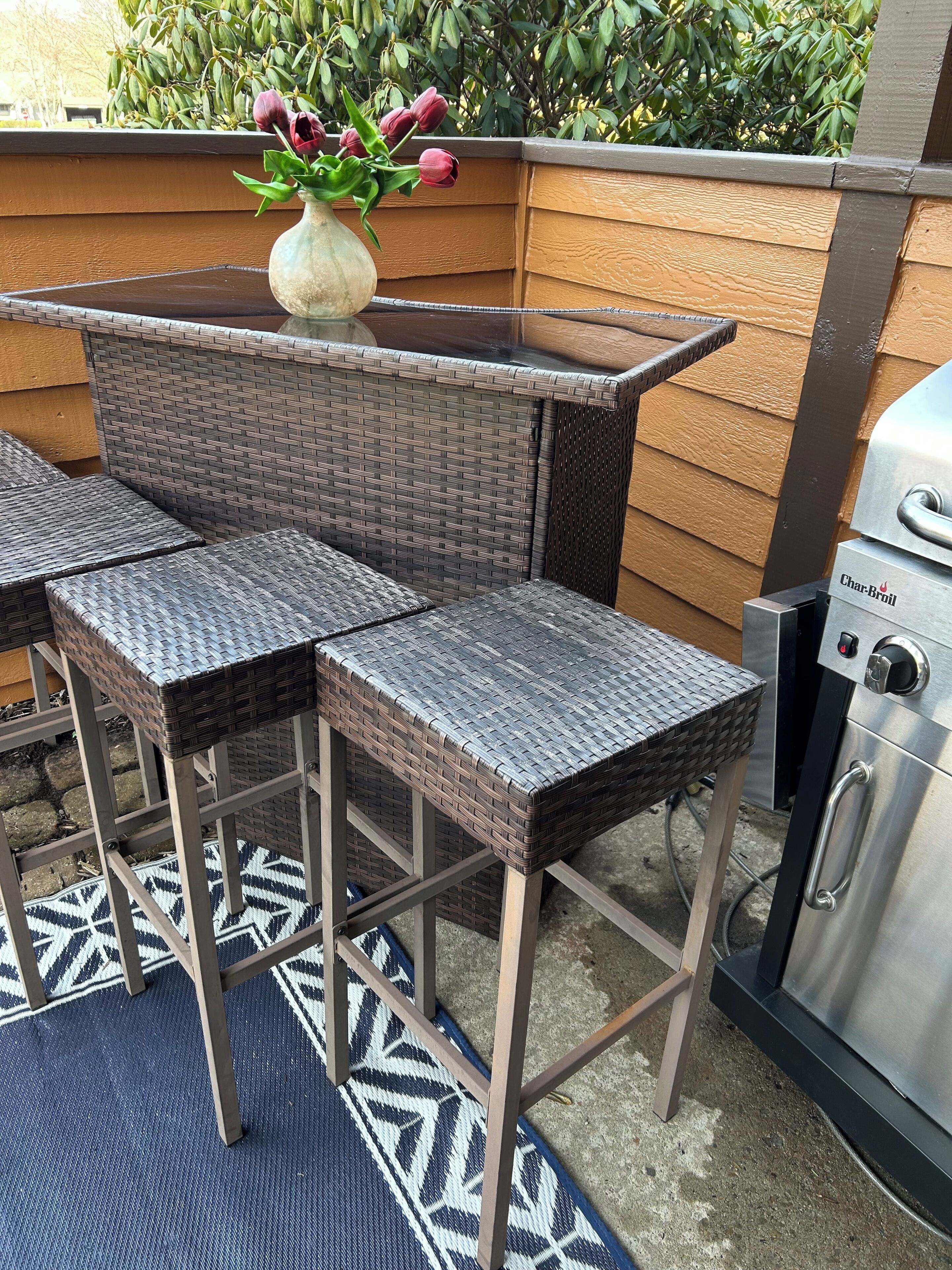 A patio area with wicker furniture, a grill, and a vase with flowers.