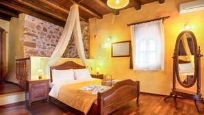 Une chambre à coucher avec un lit en bois, une table de chevet, une commode, un miroir et un mur en pierre.