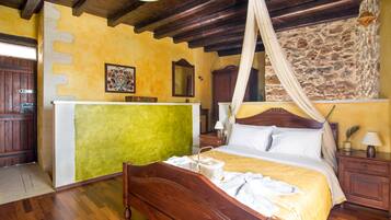 A bedroom with a wooden bed, a green accent wall, a stone wall, a wooden wardrobe, and a nightstand with a lamp.