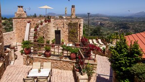 Un bâtiment en pierre doté d’une terrasse, de sièges en plein air et de plantes en pot.