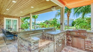 Un espacio de cocina al aire libre con encimeras de piedra, una parrilla y una mesa de comedor con sillas.