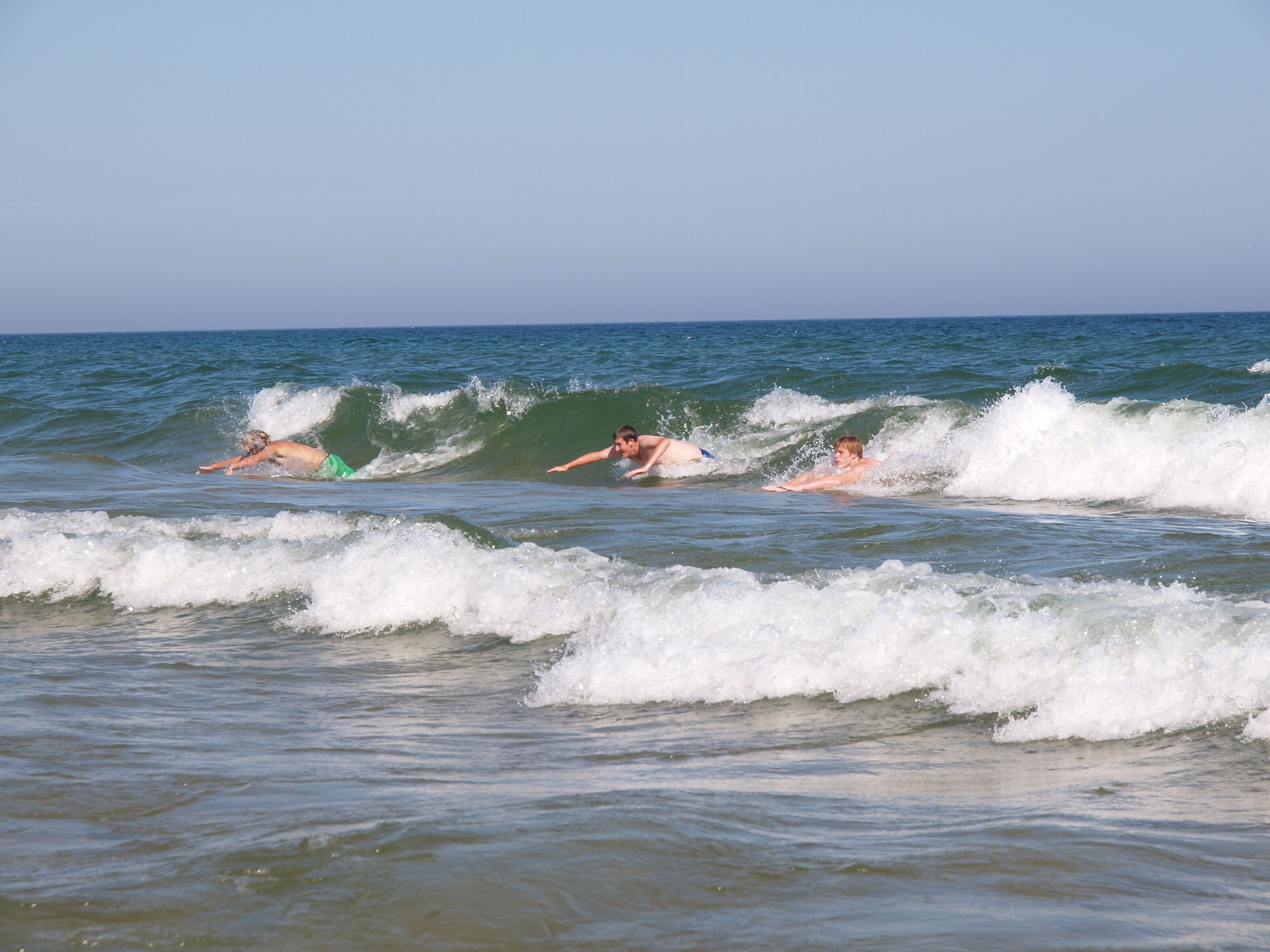 Trois personnes font de la planche à voile sur les vagues de l’océan.