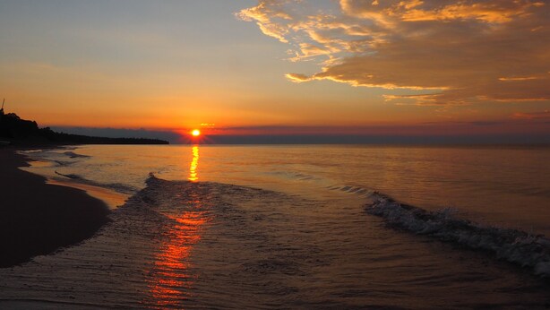 A sunset over a beach with the sun reflecting on the water. - Cozy Log Cabin ON THE WATER with the Best Sand Beach in Door County! (Sturgeon Bay)