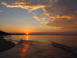A sunset over a beach with the sun reflecting on the water. - Cozy Log Cabin ON THE WATER with the Best Sand Beach in Door County! (Sturgeon Bay)