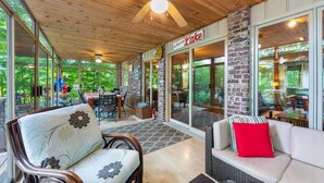 Ein überdachter Patio-Bereich mit Holzbalkendecke, großen Fenstern und Sitzgelegenheiten im Freien.