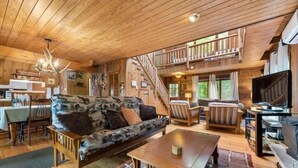 Ein Holzblockhaus-Interieur mit Wohnbereich, Essbereich und einer Treppe zu einer oberen Ebene.