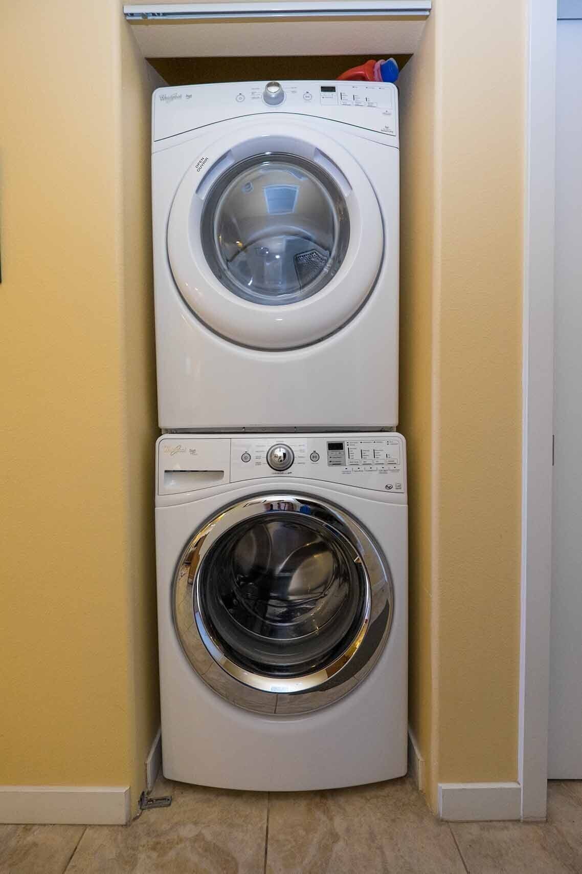 Un appareil combiné lave-linge et sèche-linge, placé dans un coin d’une pièce aux murs jaunes et au sol carrelé.
