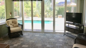 Habitación con vista a la piscina, ventilador de techo y televisor sobre un soporte.