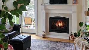 Ett vardagsrum med en öppen spis, en takfläkt och en tv som står på en hylla ovanför spisen.