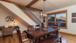 A dining area with a wooden table, chairs, and a staircase with exposed beams.