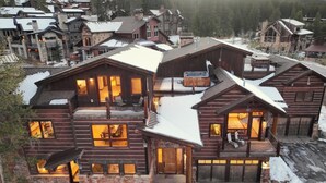 A large log cabin with multiple levels, outdoor seating, and a stone foundation.