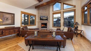A spacious living room with a fireplace, large windows, and a stone fireplace surround.