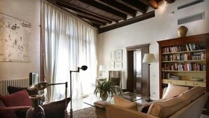 Ein gemütliches Wohnzimmer mit Sofa, Couchtisch, Bücherregal und einem großen Fenster mit Vorhängen.