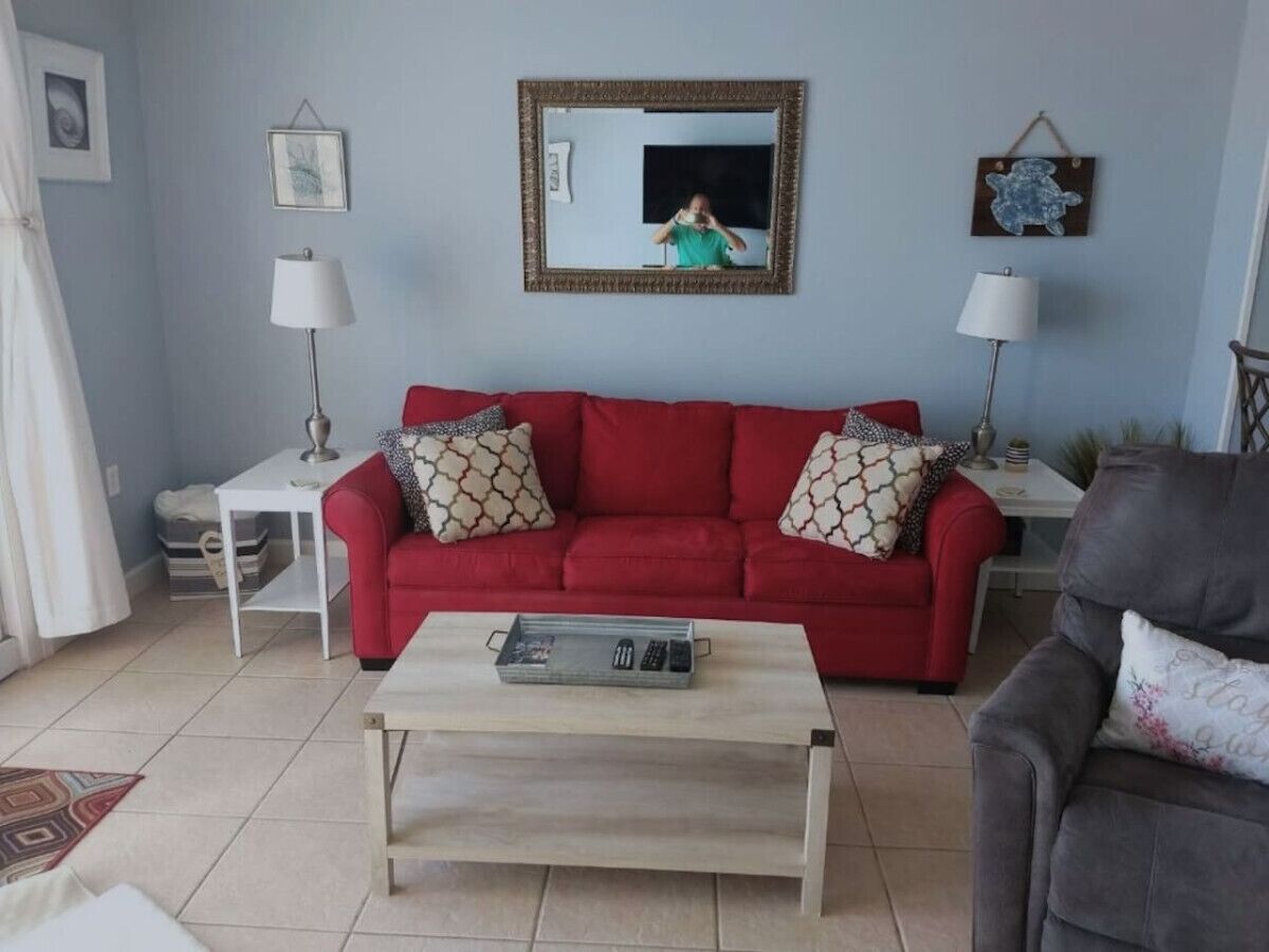 Uma sala de estar com um sofá vermelho, duas mesas laterais, uma mesa de centro e um espelho na parede.