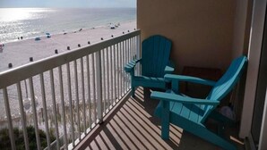 A balcony with a view of the beach, featuring two blue Adirondack chairs.