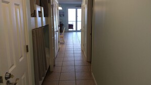 A hallway with a tiled floor, doors on the left, and a window at the end.