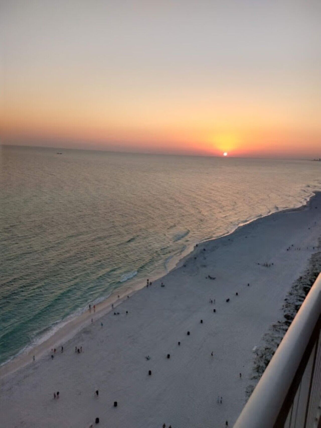 A beach with people walking along the shore during sunset.