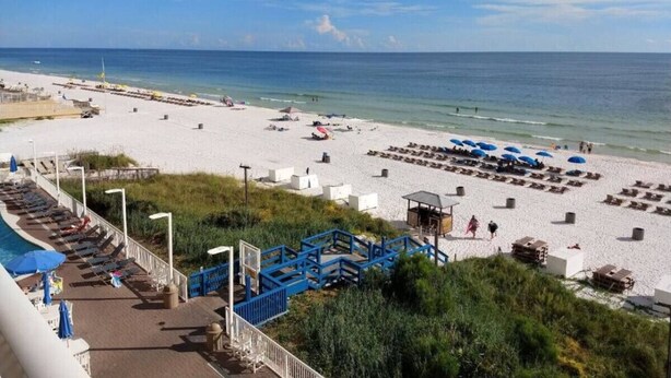 A beach with sun loungers, umbrellas, and a pool area.