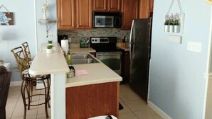 A kitchen with wooden cabinets, a microwave, stove, and refrigerator. There is a small island with a sink and bar stools.