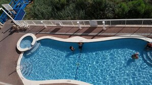 An aerial view of a swimming pool with a curved edge, surrounded by a white deck and a white fence.