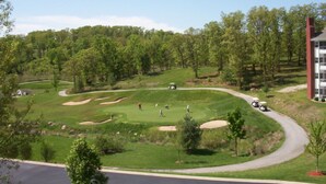 A golf course with sand bunkers, a parking area, and a building with a red facade.