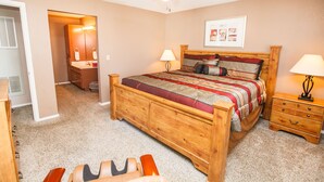 A bedroom with a wooden bed, a nightstand, a dresser, a ceiling fan, and a door leading to another room.