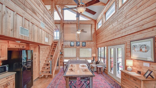 A spacious wooden cabin with a dining area, kitchen, and a staircase leading to an upper level. - Mata'Zamo cliffside cabin, 1000 acres hiking trails, farm animals, family fun! (Glen Rose)