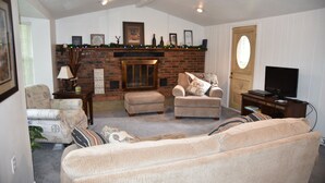Un salón con chimenea, dos sillones, un sofá, un televisor y una estantería.