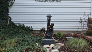 Un letrero de bienvenida con una lámpara decorativa y dos estatuas de niños frente a una casa.
