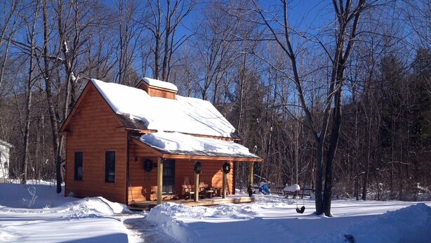Una cabaña de madera con un porche, rodeada de nieve y árboles.