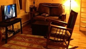 Una sala de estar acogedora con televisor, sofá de cuero, mecedora de madera y un tapete estampado.