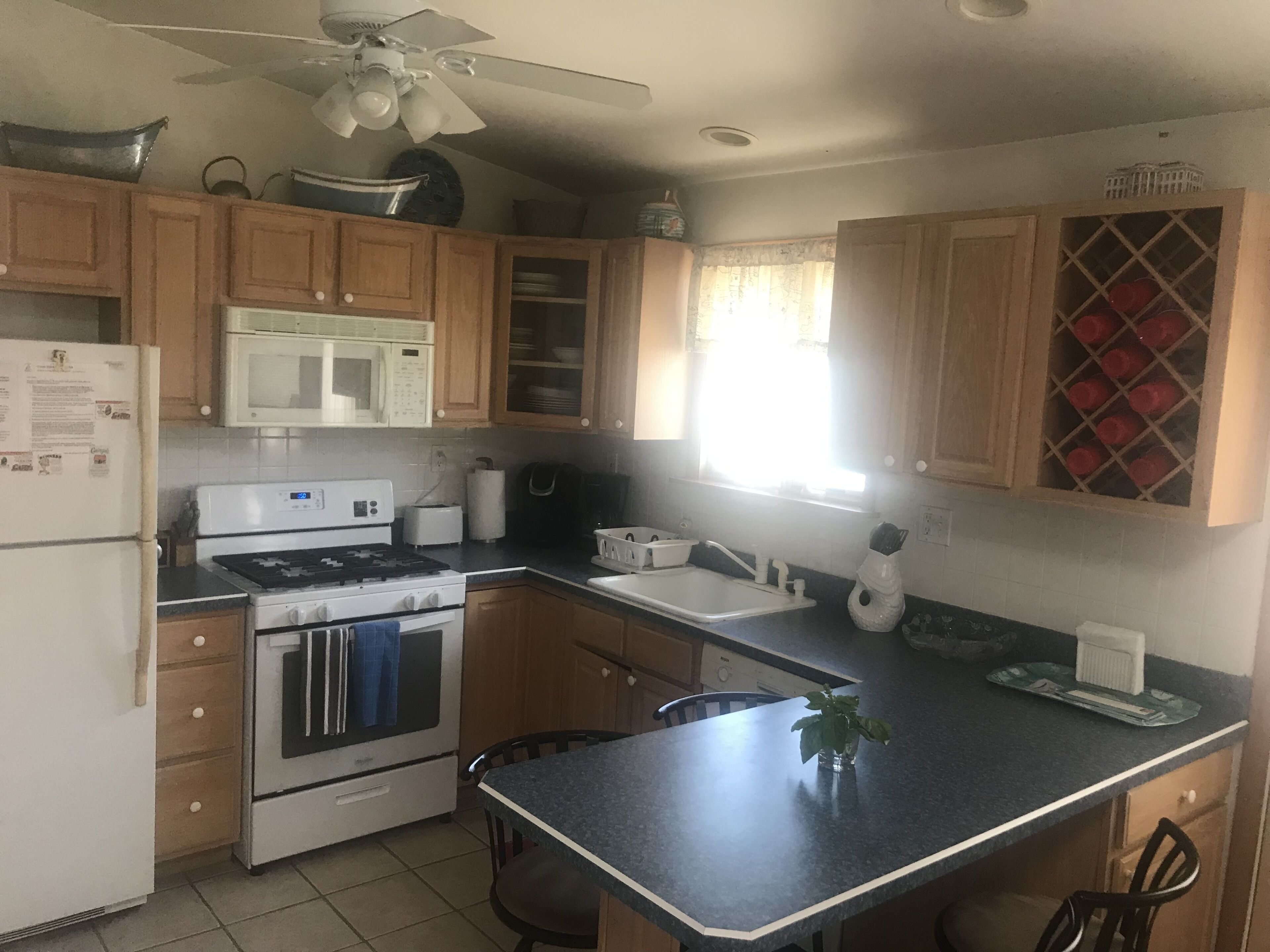 A kitchen with wooden cabinets, a microwave, stove, sink, and a ceiling fan.