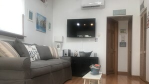 Un soggiorno moderno con un divano grigio, una TV a schermo piatto montata a parete, un piccolo tavolino bianco con un secchio e un pavimento in legno.