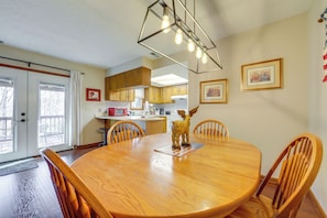 A dining area with a wooden table, chairs, and a decorative moose figure. There is a kitchen in the background with wooden cabinets and a red appliance.