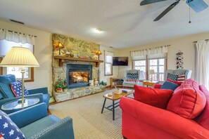 A living room with a stone fireplace, a ceiling fan, and a red sofa.