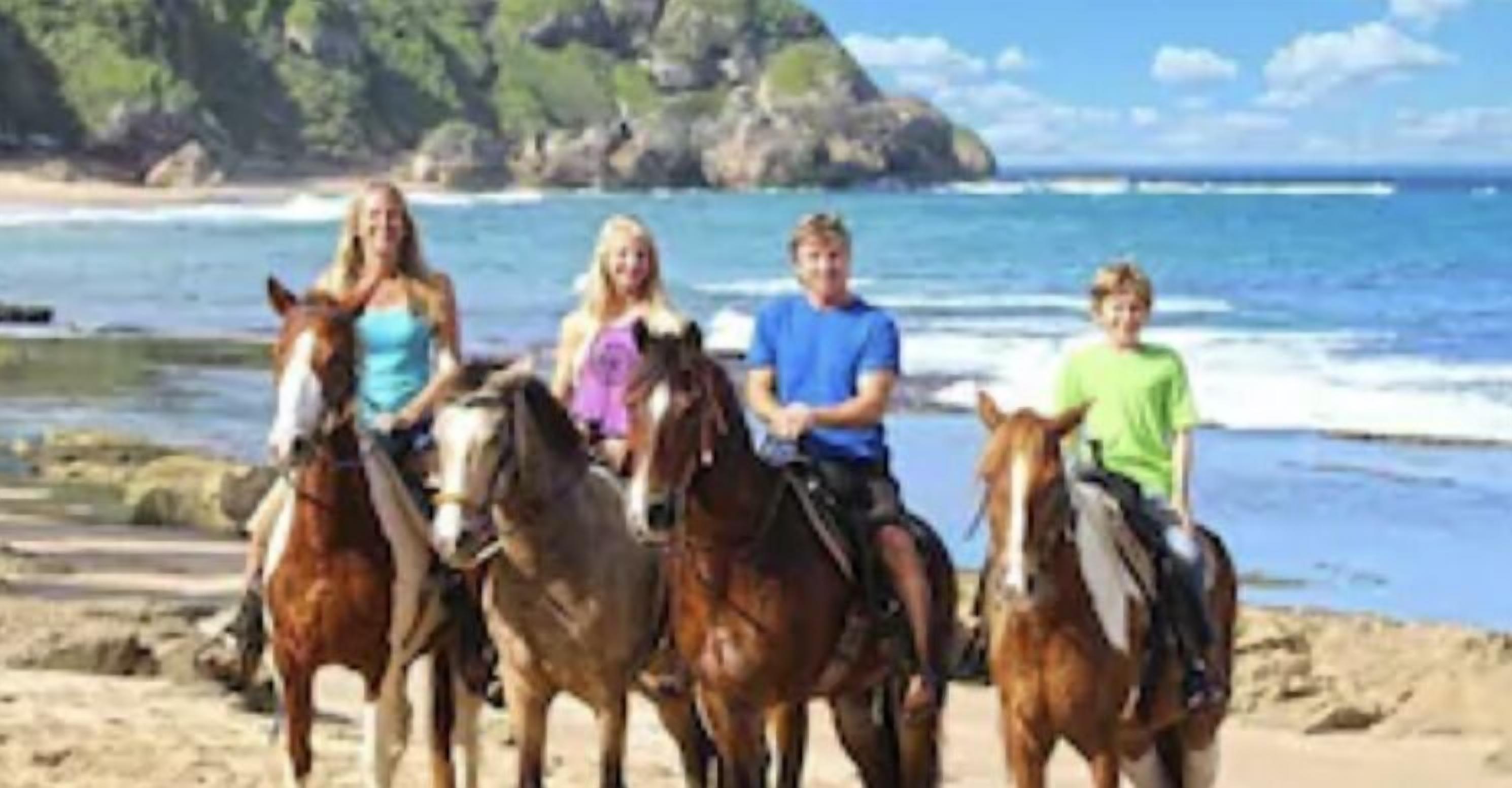 Eine Strandansicht, auf der Personen zu Pferd reiten.