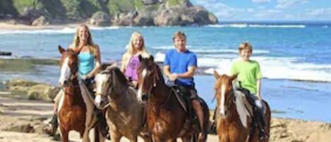 Eine Strandansicht, auf der Personen zu Pferd reiten.