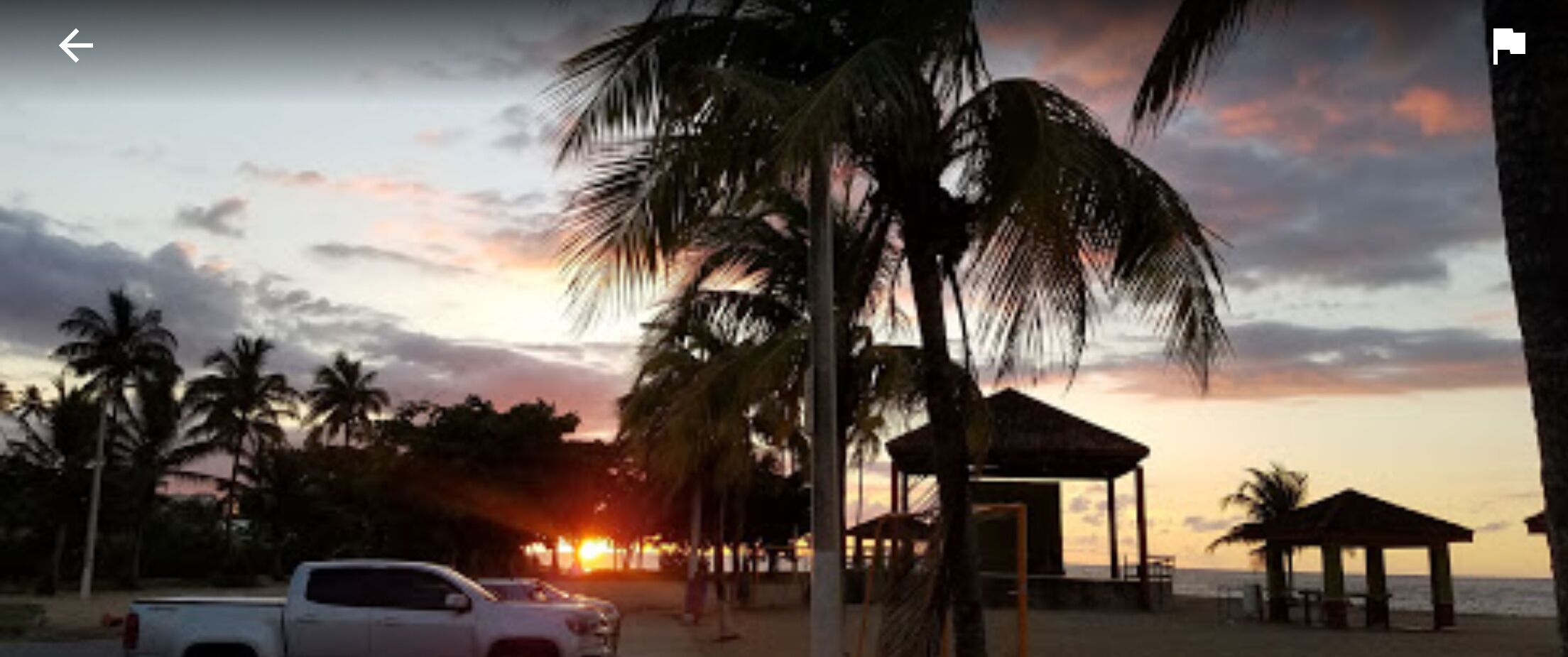 A beach scene with palm trees, a gazebo, and a sunset.