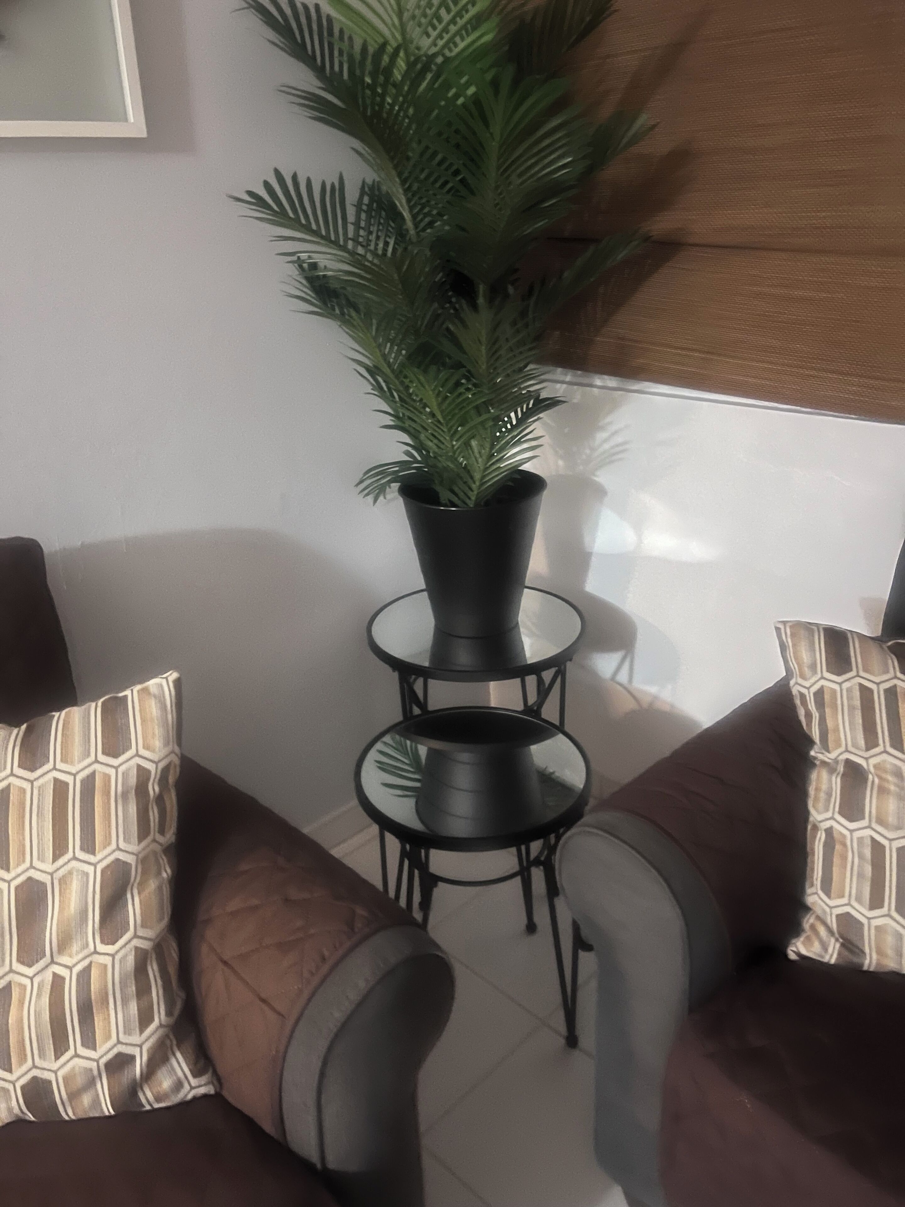 Et hjørne af et rum med en brun sofa, et lille rundt bord med en potteplante og mønstrede puder.