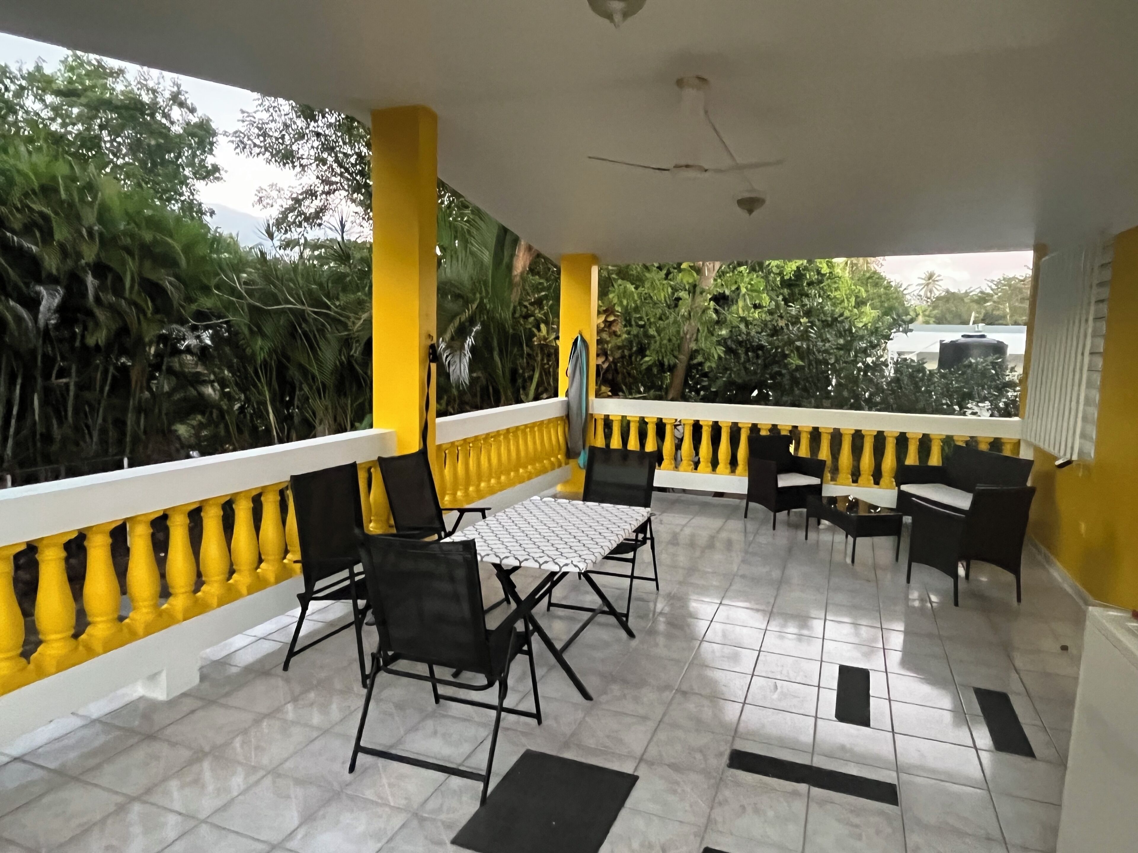 A covered outdoor seating area with yellow railings, black chairs, and a tiled floor.