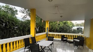 A covered outdoor seating area with yellow railings, black chairs, and a tiled floor.