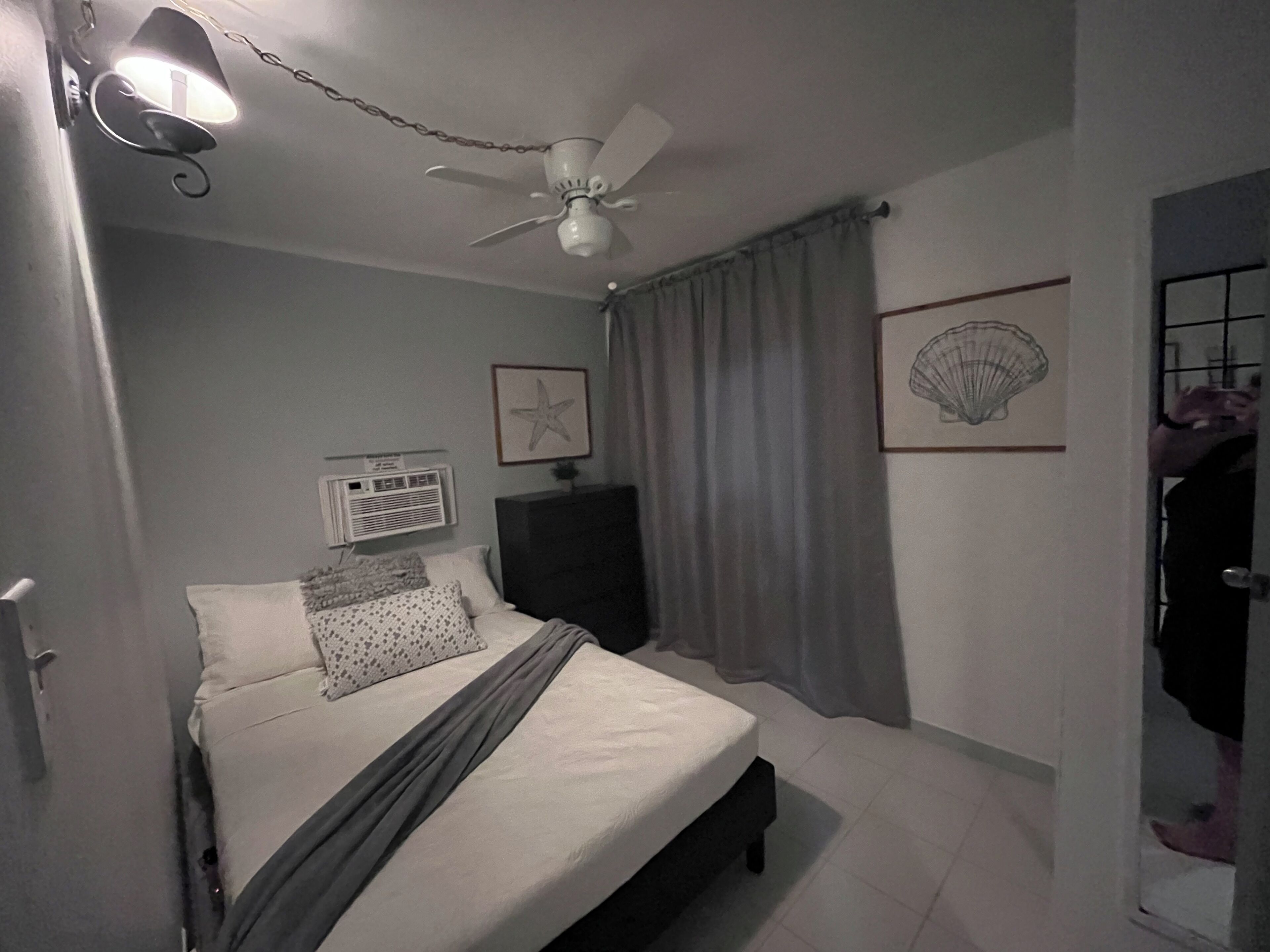 Un dormitorio con cama, ventilador de techo, aire acondicionado de pared y una puerta que da a otra habitación.