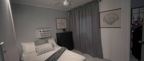 Un dormitorio con cama, ventilador de techo, aire acondicionado de pared y una puerta que da a otra habitación.