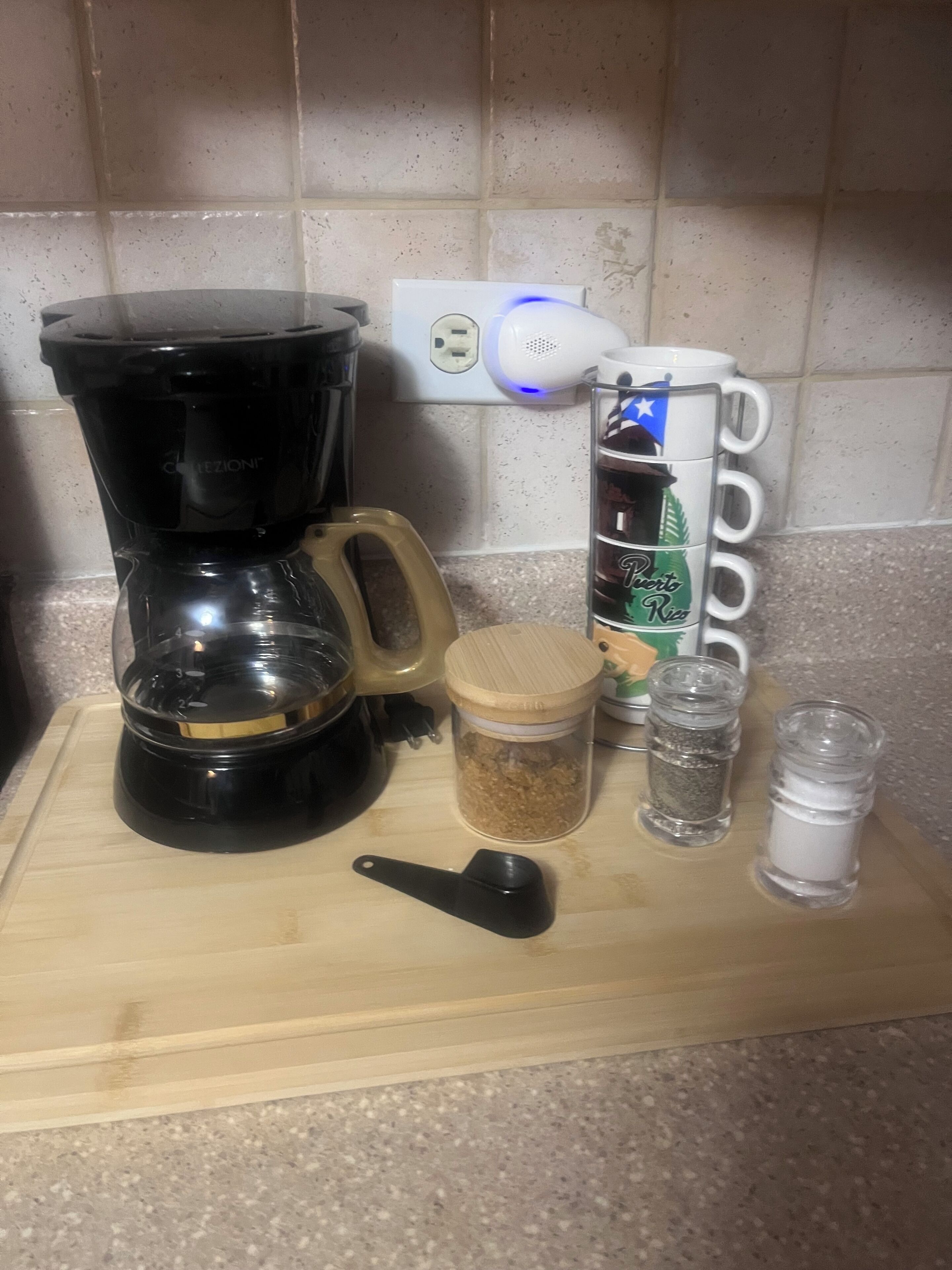 A kitchen counter with a coffee maker, a jar of sugar, a salt shaker, and a mug.