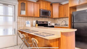 A kitchen with wooden cabinets, a stainless steel microwave, a black refrigerator, and a bar area with stools.