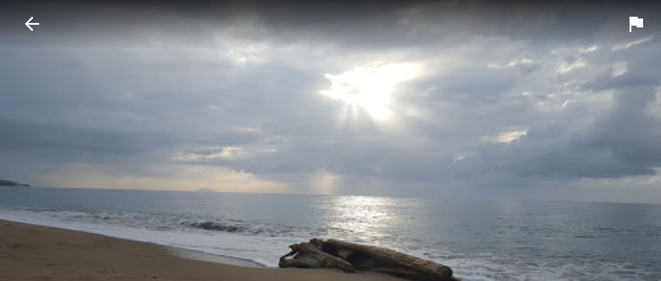 A beach with a large rock in the foreground and the ocean in the background.