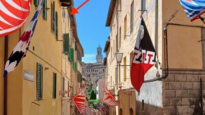 Una calle estrecha flanqueada por edificios, un cartel de no estacionamiento y banderas colgadas de los edificios.