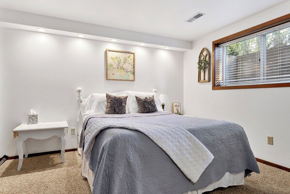 A bedroom with a bed, bedside table, and a window with blinds. - Clean, Quiet Farm Apartment | 117 Acres, Hot Tub, Private Patio & Views (Lynden)